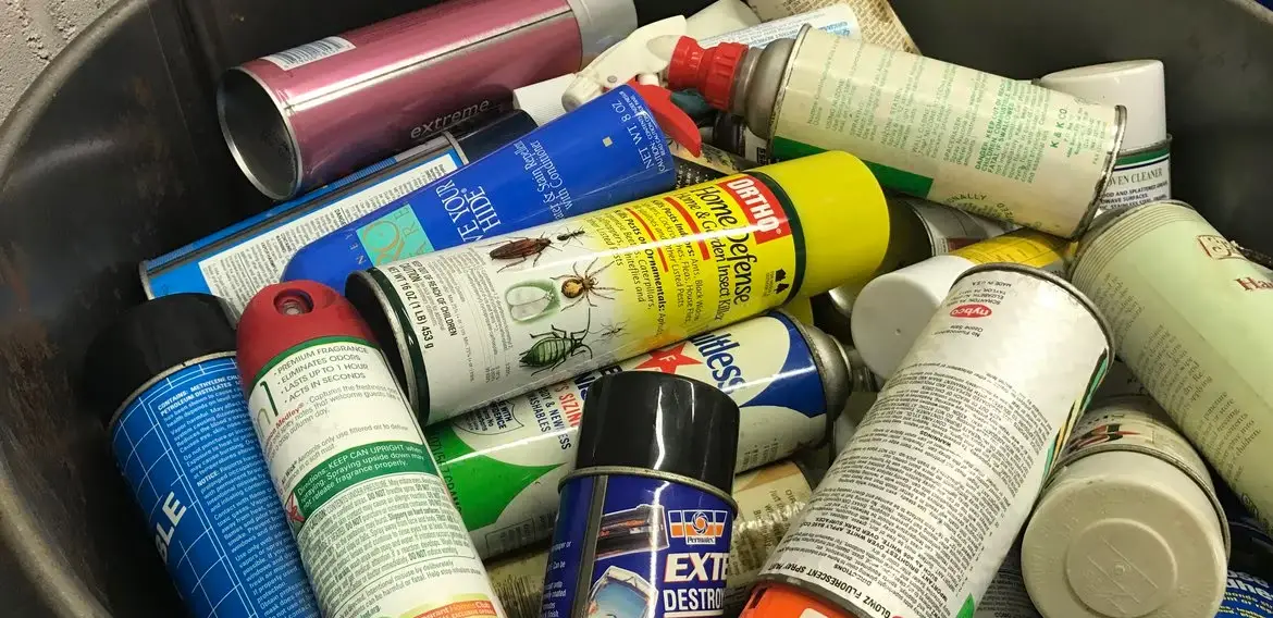 Image of presumably empty aerosol cans strewn across a garbage bin